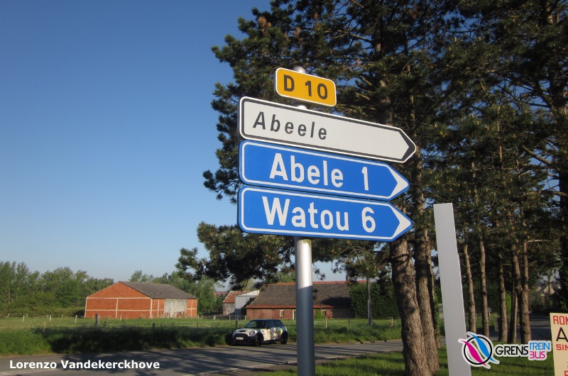 Een Franse wegwijzer 'Abeele' en daaronder twee Belgische wegwijzers.